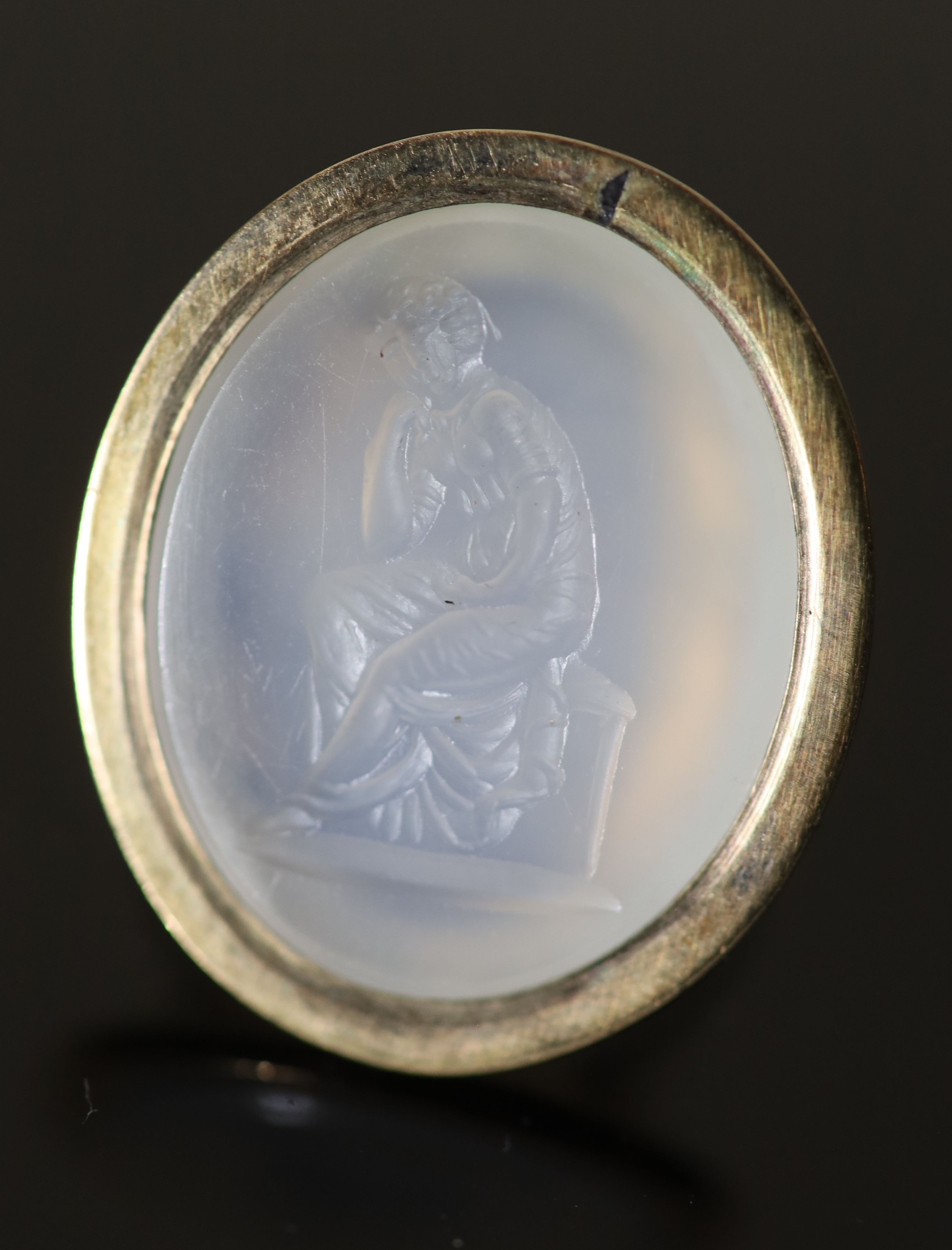 An early 19th century gold and white agate oval intaglio ring, carved with a seated figure,